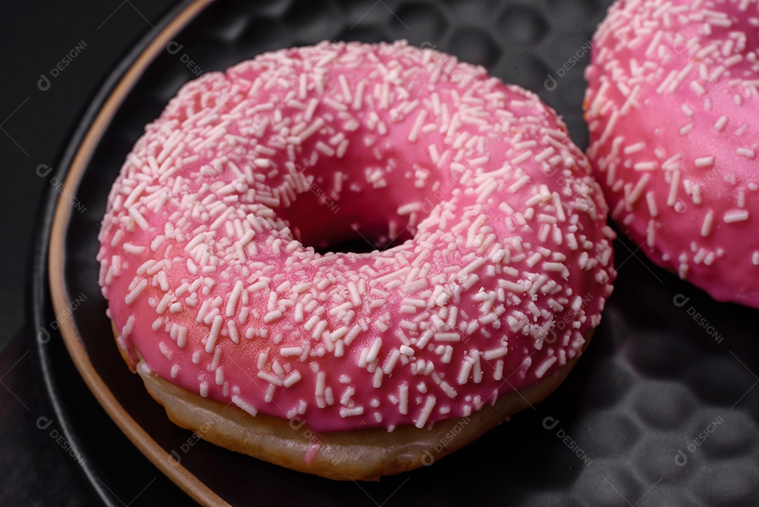 Deliciosos donuts doces frescos em esmalte rosa com recheio de morango sobre um fundo escuro de concreto
