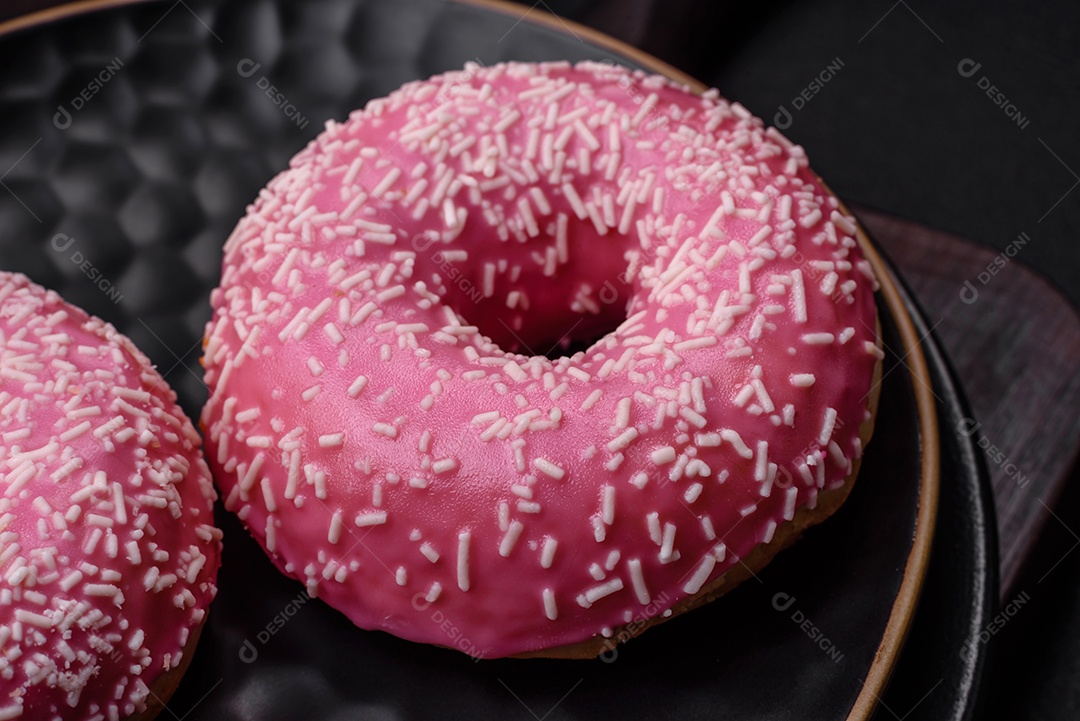 Deliciosos donuts doces frescos em esmalte rosa com recheio de morango sobre um fundo escuro de concreto