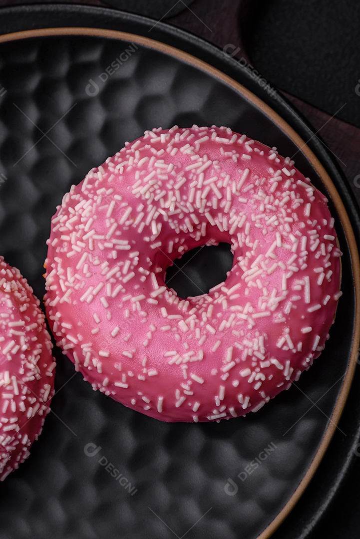 Deliciosos donuts doces frescos em esmalte rosa com recheio de morango sobre um fundo escuro de concreto