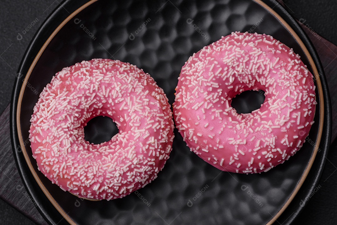 Deliciosos donuts doces frescos em esmalte rosa com recheio de morango sobre um fundo escuro de concreto