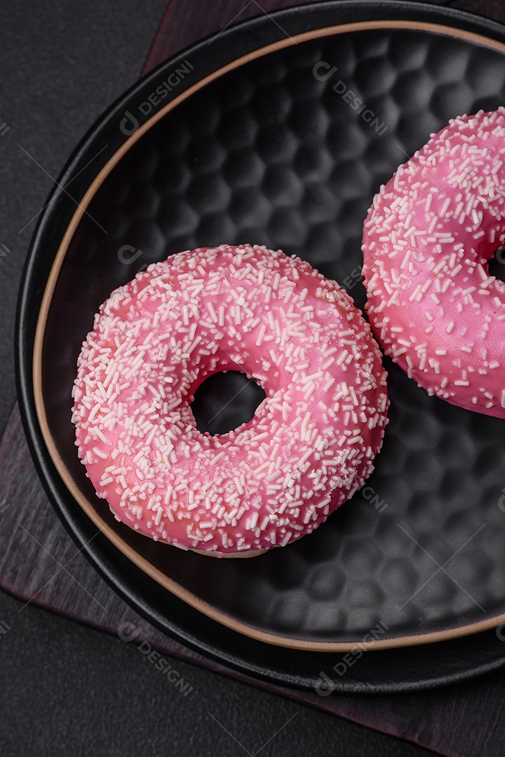 Deliciosos donuts doces frescos em esmalte rosa com recheio de morango sobre um fundo escuro de concreto