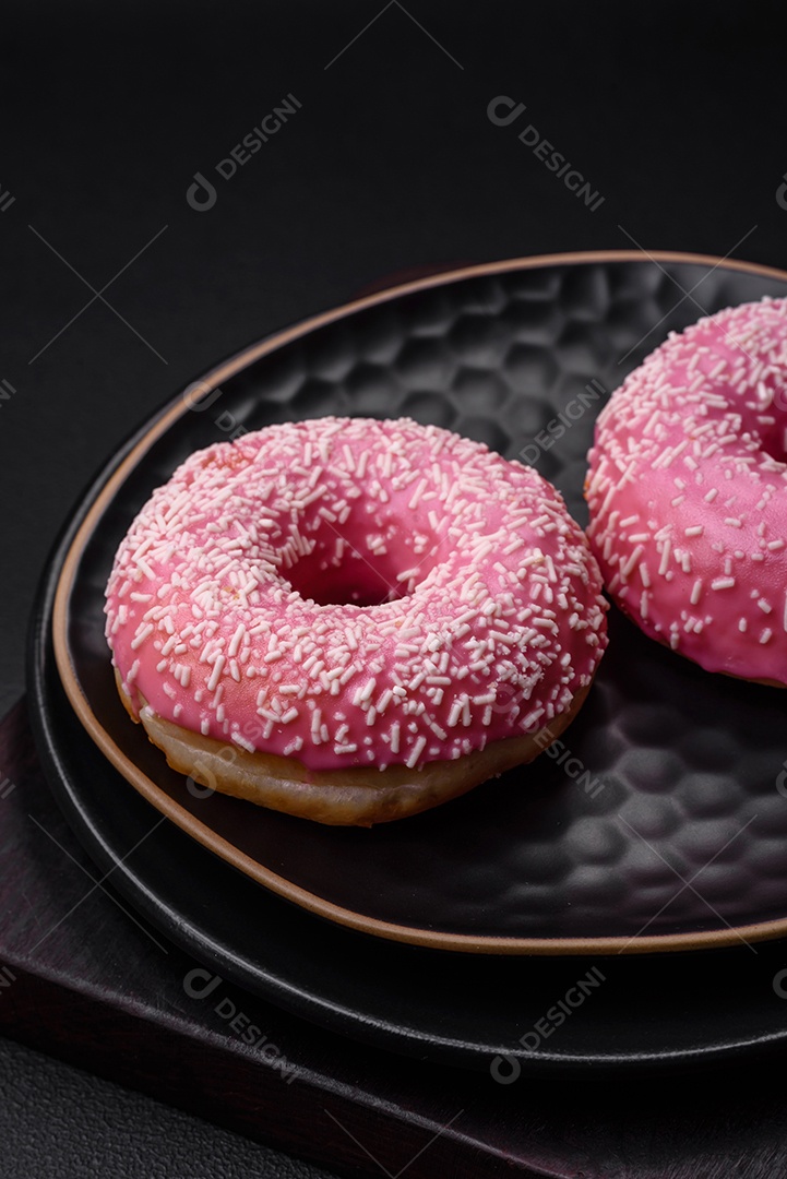 Deliciosos donuts doces frescos em esmalte rosa com recheio de morango sobre um fundo escuro de concreto