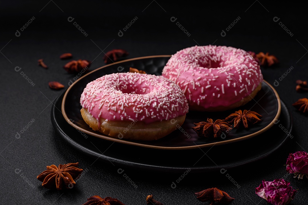 Deliciosos donuts doces frescos em esmalte rosa com recheio de morango sobre um fundo escuro de concreto