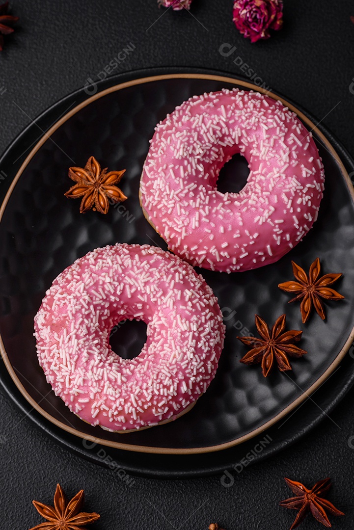 Deliciosos donuts doces frescos em esmalte rosa com recheio de morango sobre um fundo escuro de concreto