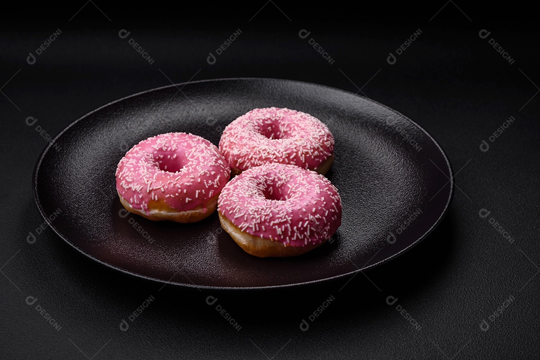 Deliciosos donuts doces frescos em esmalte rosa com recheio de morango sobre um fundo escuro de concreto