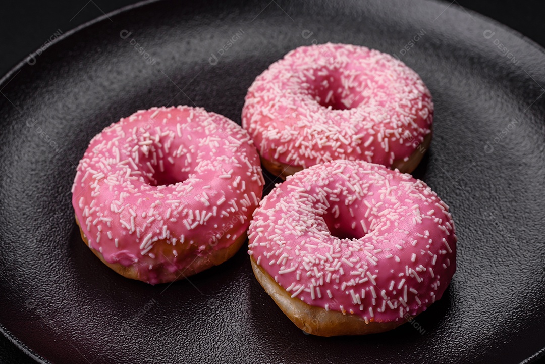 Deliciosos donuts doces frescos em esmalte rosa com recheio de morango sobre um fundo escuro de concreto