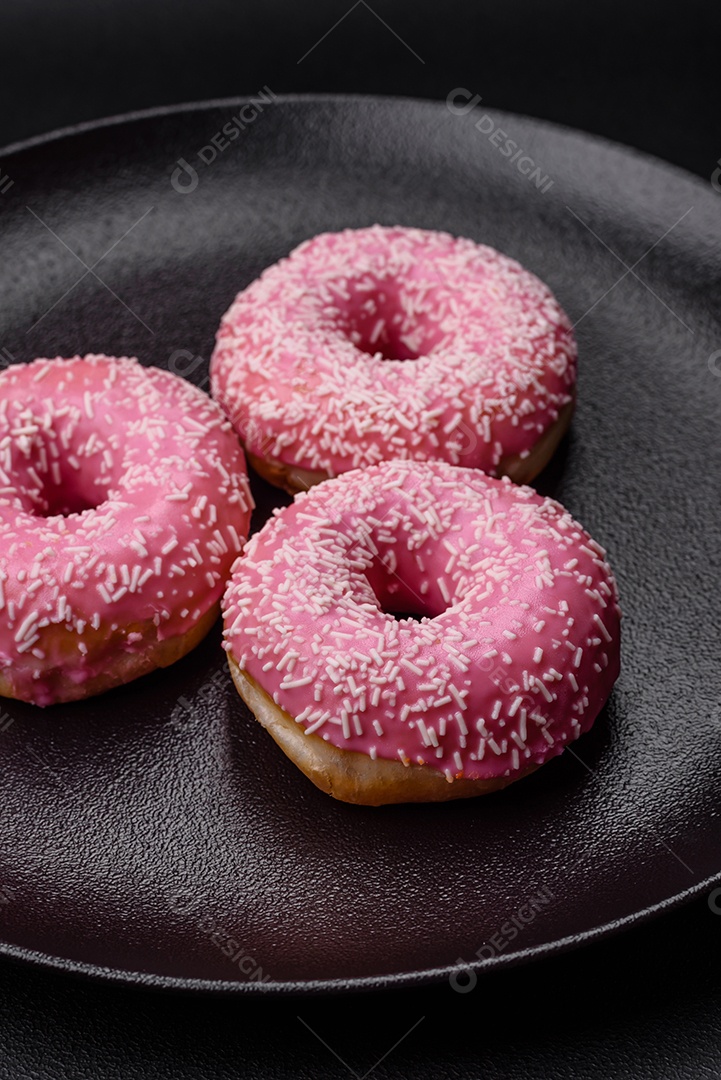 Deliciosos donuts doces frescos em esmalte rosa com recheio de morango sobre um fundo escuro de concreto