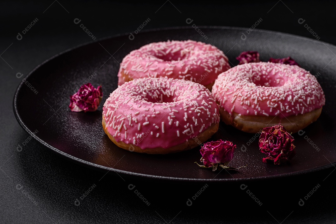 Deliciosos donuts doces frescos em esmalte rosa com recheio de morango sobre um fundo escuro de concreto