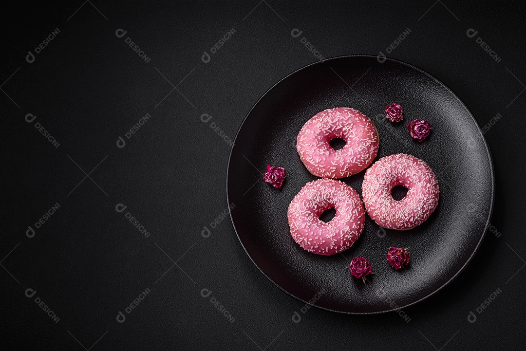Deliciosos donuts doces frescos em esmalte rosa com recheio de morango sobre um fundo escuro de concreto