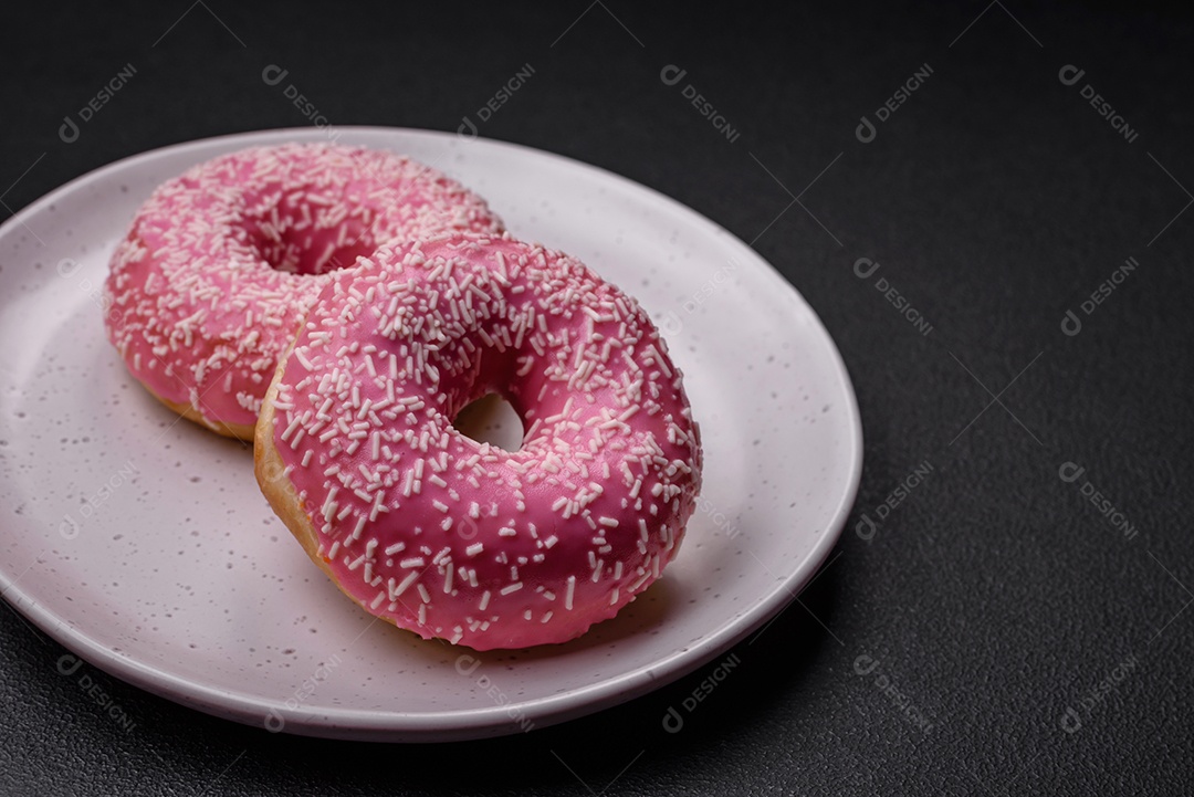 Deliciosos donuts doces frescos em esmalte rosa com recheio de morango sobre um fundo escuro de concreto