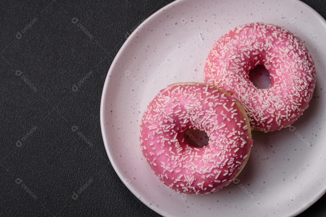 Deliciosos donuts doces frescos em esmalte rosa com recheio de morango sobre um fundo escuro de concreto