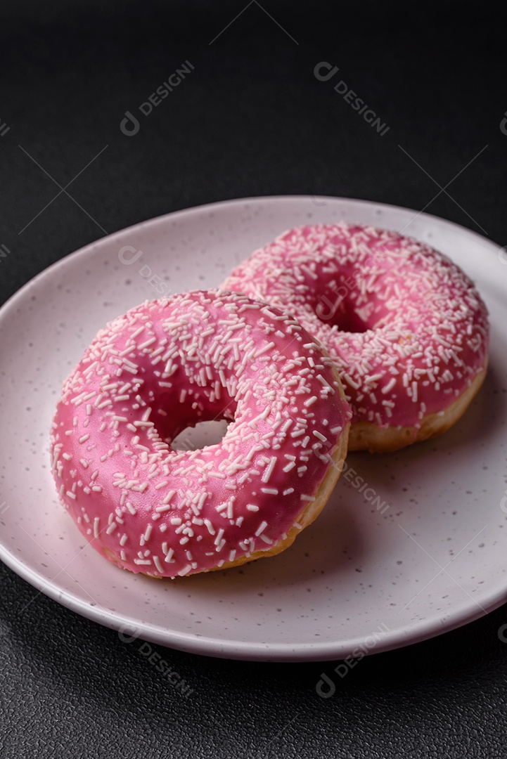 Deliciosos donuts doces frescos em esmalte rosa com recheio de morango sobre um fundo escuro de concreto