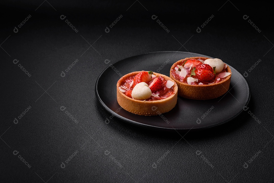 Deliciosas tortinhas doces frescas com morangos e flocos de coco sobre um fundo escuro de concreto