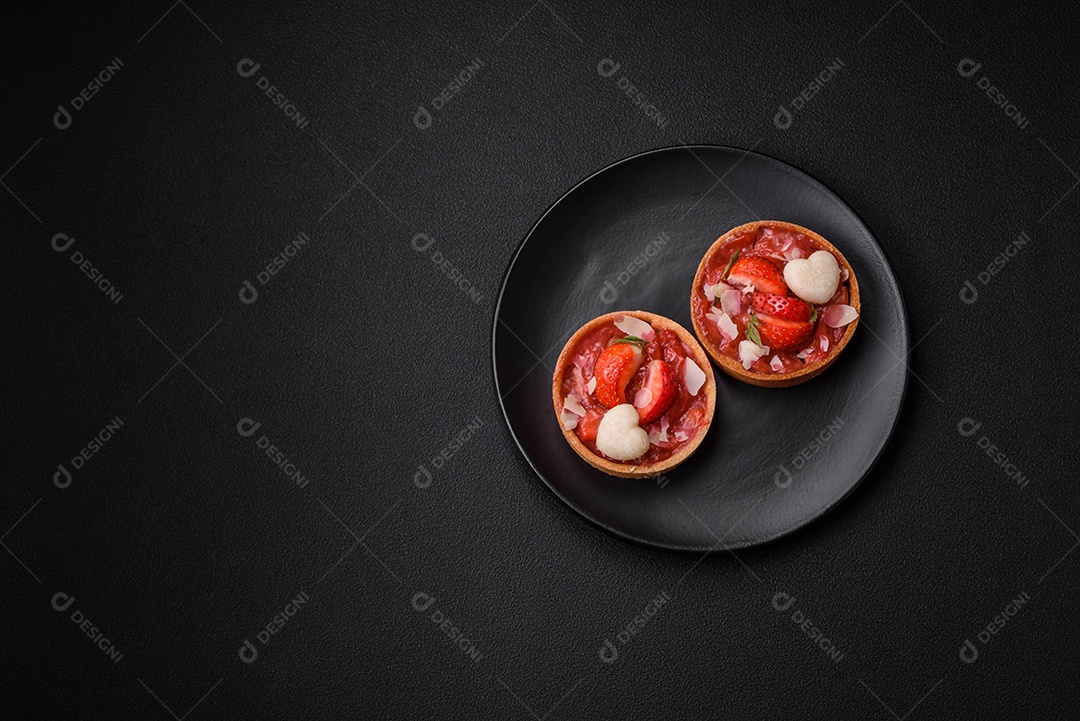 Deliciosas tortinhas doces frescas com morangos e flocos de coco sobre um fundo escuro de concreto