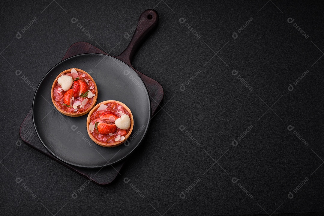 Deliciosas tortinhas doces frescas com morangos e flocos de coco sobre um fundo escuro de concreto