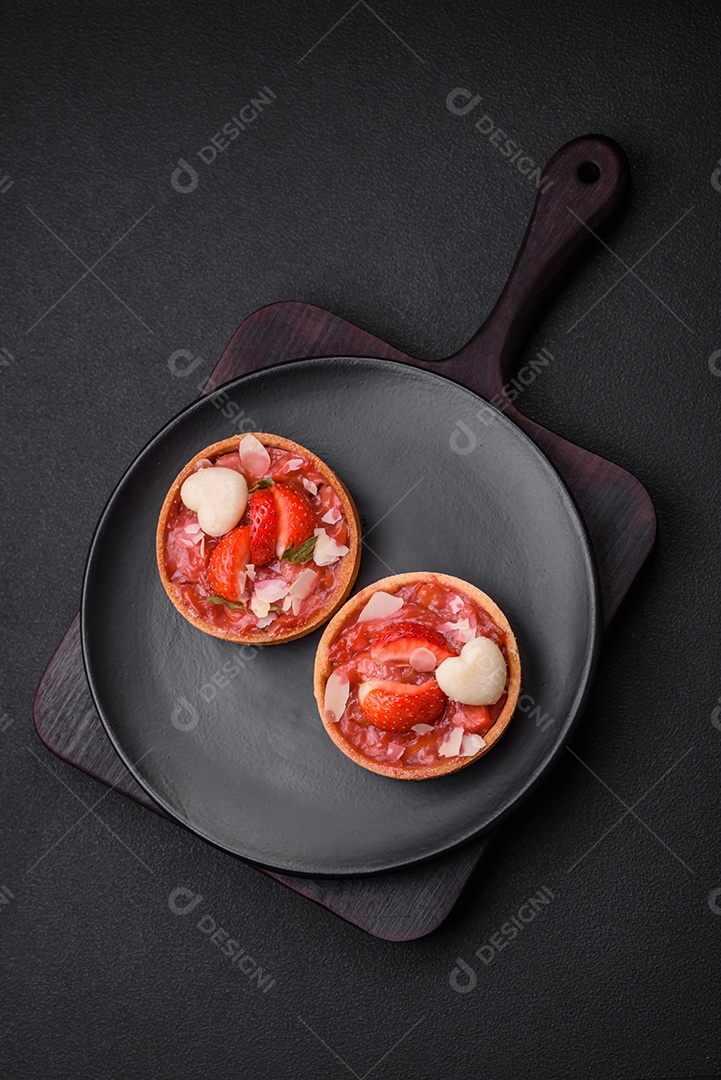 Deliciosas tortinhas doces frescas com morangos e flocos de coco sobre um fundo escuro de concreto