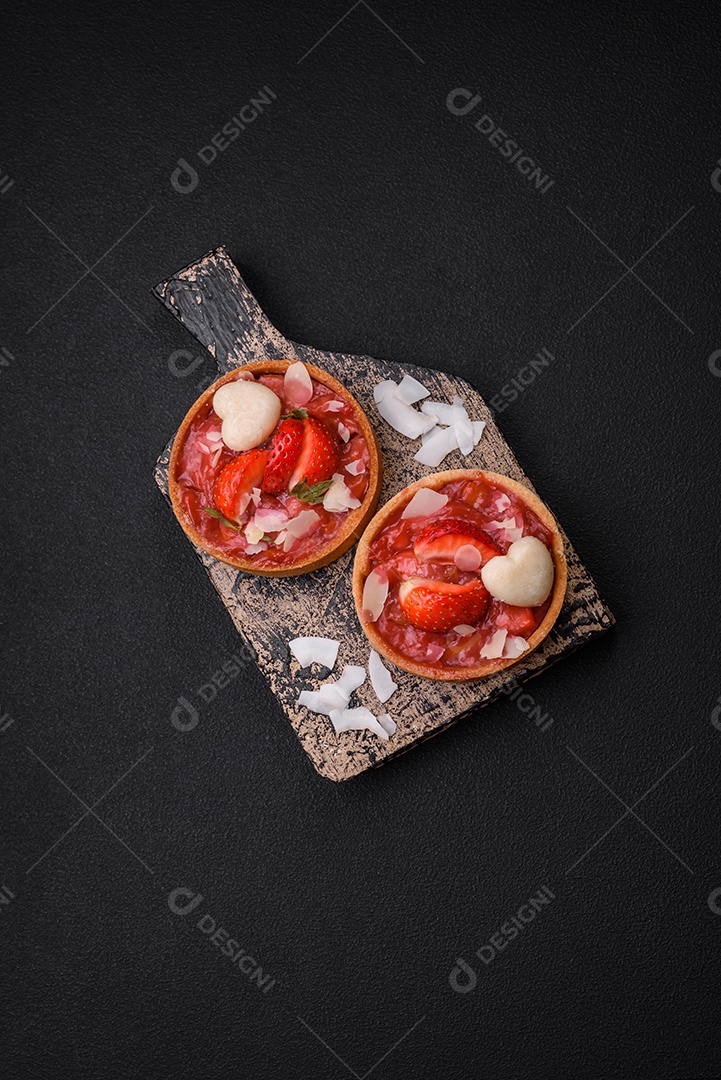 Deliciosas tortinhas doces frescas com morangos e flocos de coco sobre um fundo escuro de concreto