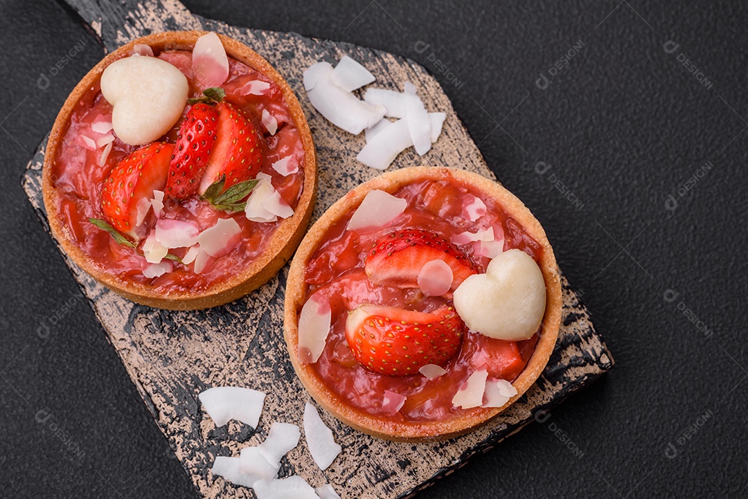 Deliciosas tortinhas doces frescas com morangos e flocos de coco sobre um fundo escuro de concreto