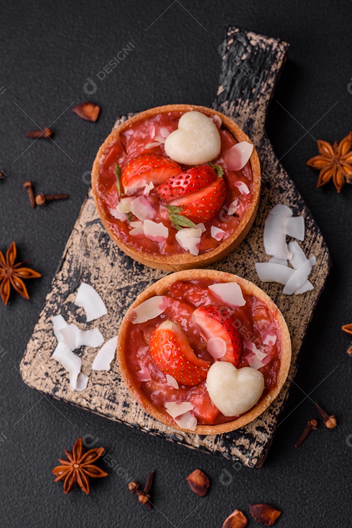 Deliciosas tortinhas doces frescas com morangos e flocos de coco sobre um fundo escuro de concreto