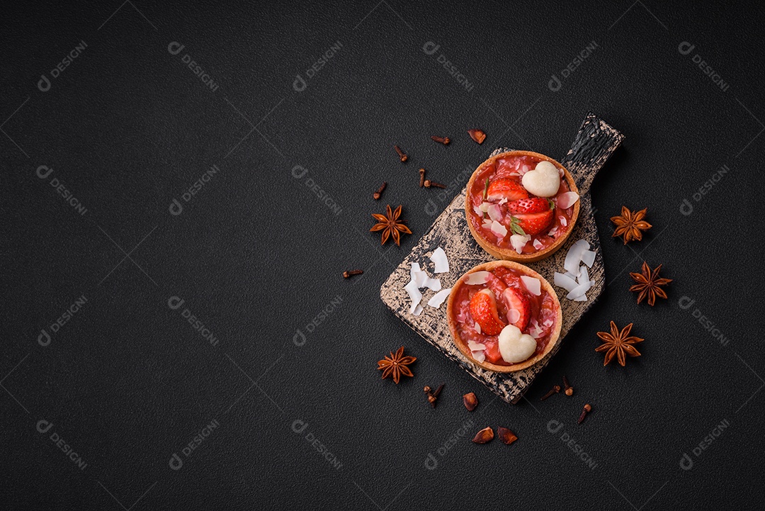 Deliciosas tortinhas doces frescas com morangos e flocos de coco sobre um fundo escuro de concreto