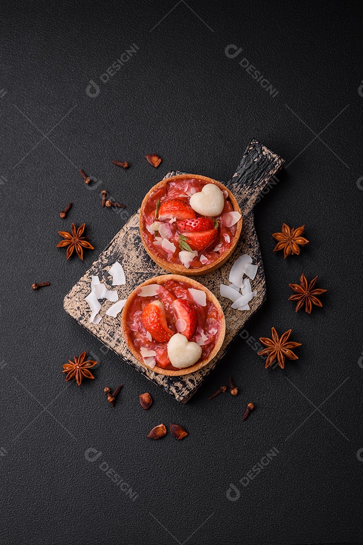 Deliciosas tortinhas doces frescas com morangos e flocos de coco sobre um fundo escuro de concreto