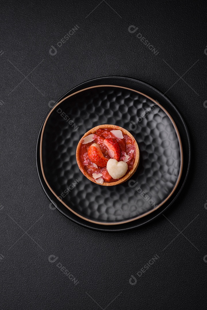 Deliciosas tortinhas doces frescas com morangos e flocos de coco sobre um fundo escuro de concreto