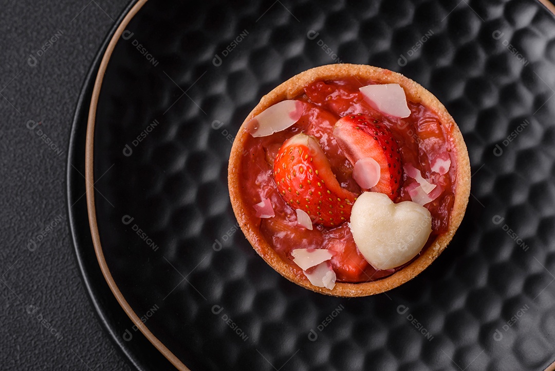 Deliciosas tortinhas doces frescas com morangos e flocos de coco sobre um fundo escuro de concreto