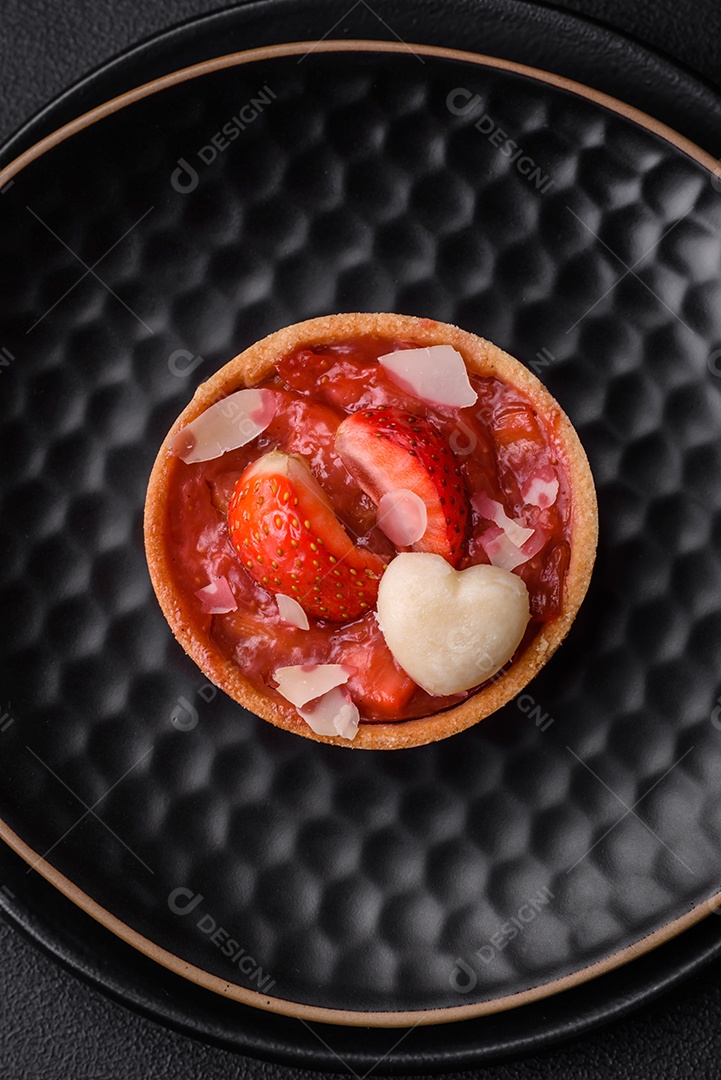 Deliciosas tortinhas doces frescas com morangos e flocos de coco sobre um fundo escuro de concreto