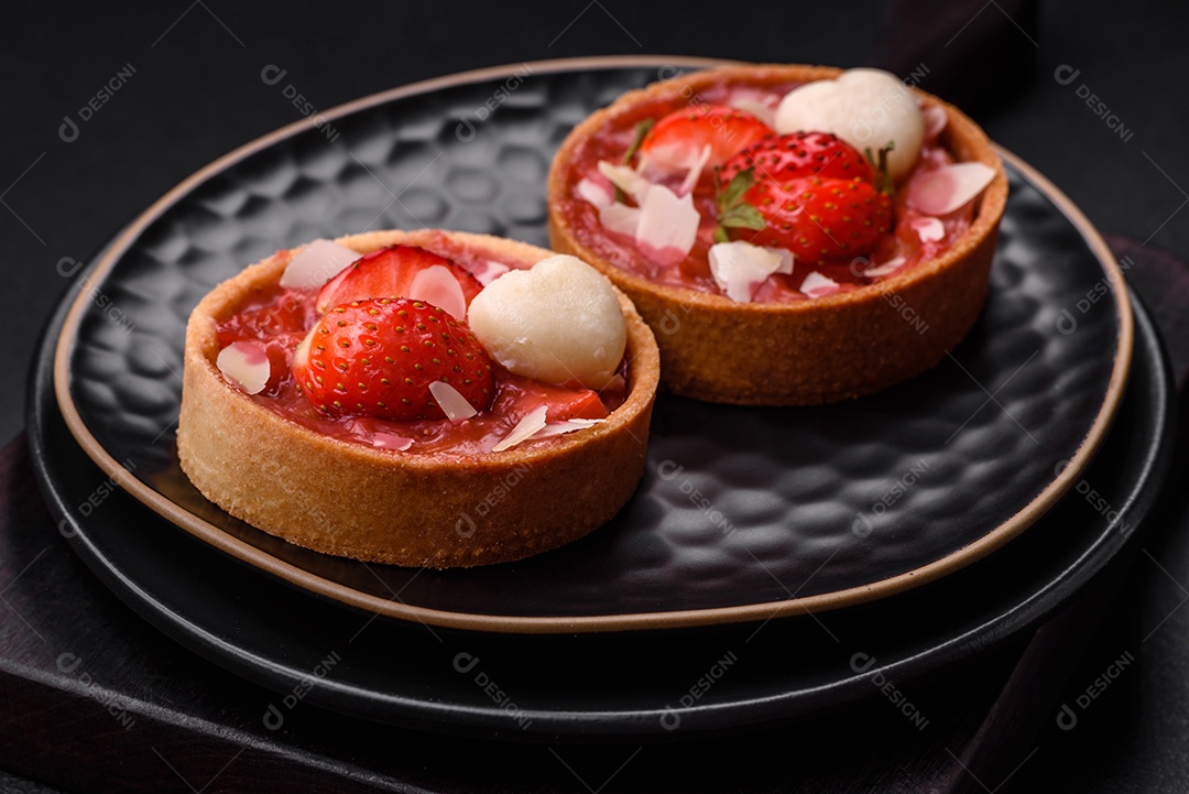 Deliciosas tortinhas doces frescas com morangos e flocos de coco sobre um fundo escuro de concreto