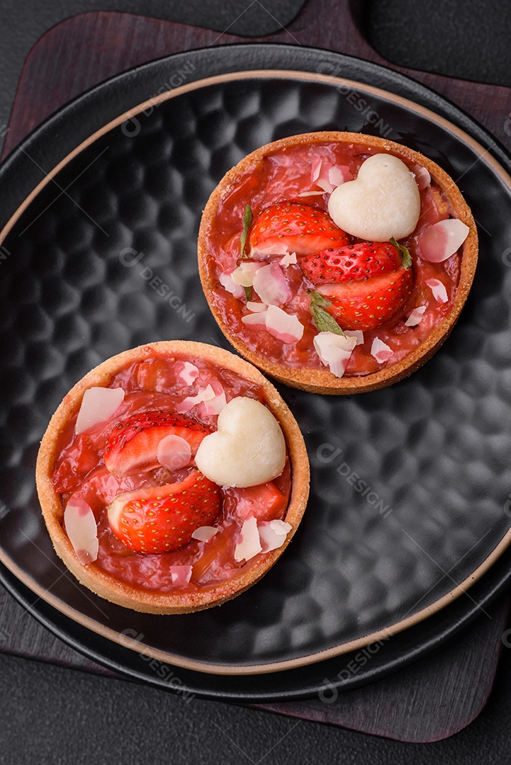 Deliciosas tortinhas doces frescas com morangos e flocos de coco sobre um fundo escuro de concreto