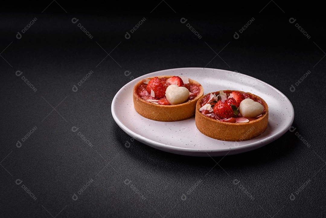 Deliciosas tortinhas doces frescas com morangos e flocos de coco sobre um fundo escuro de concreto