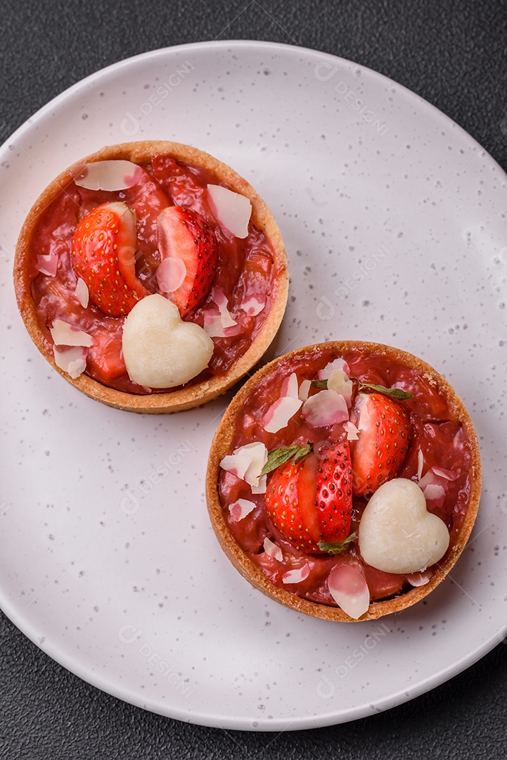 Deliciosas tortinhas doces frescas com morangos e flocos de coco sobre um fundo escuro de concreto