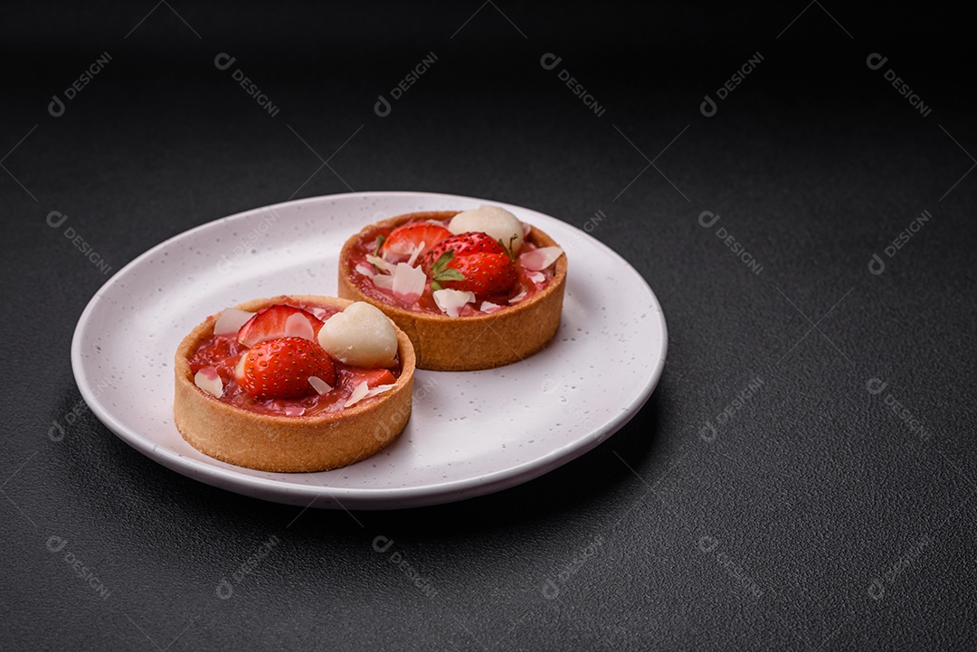 Deliciosas tortinhas doces frescas com morangos e flocos de coco sobre um fundo escuro de concreto