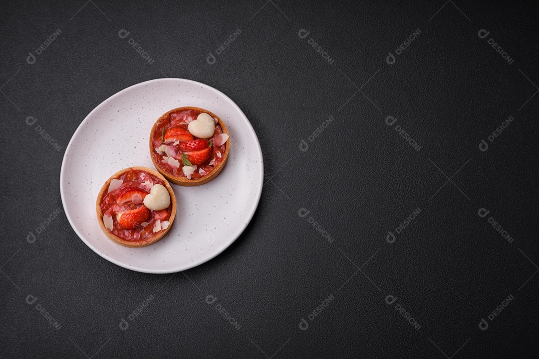 Deliciosas tortinhas doces frescas com morangos e flocos de coco sobre um fundo escuro de concreto
