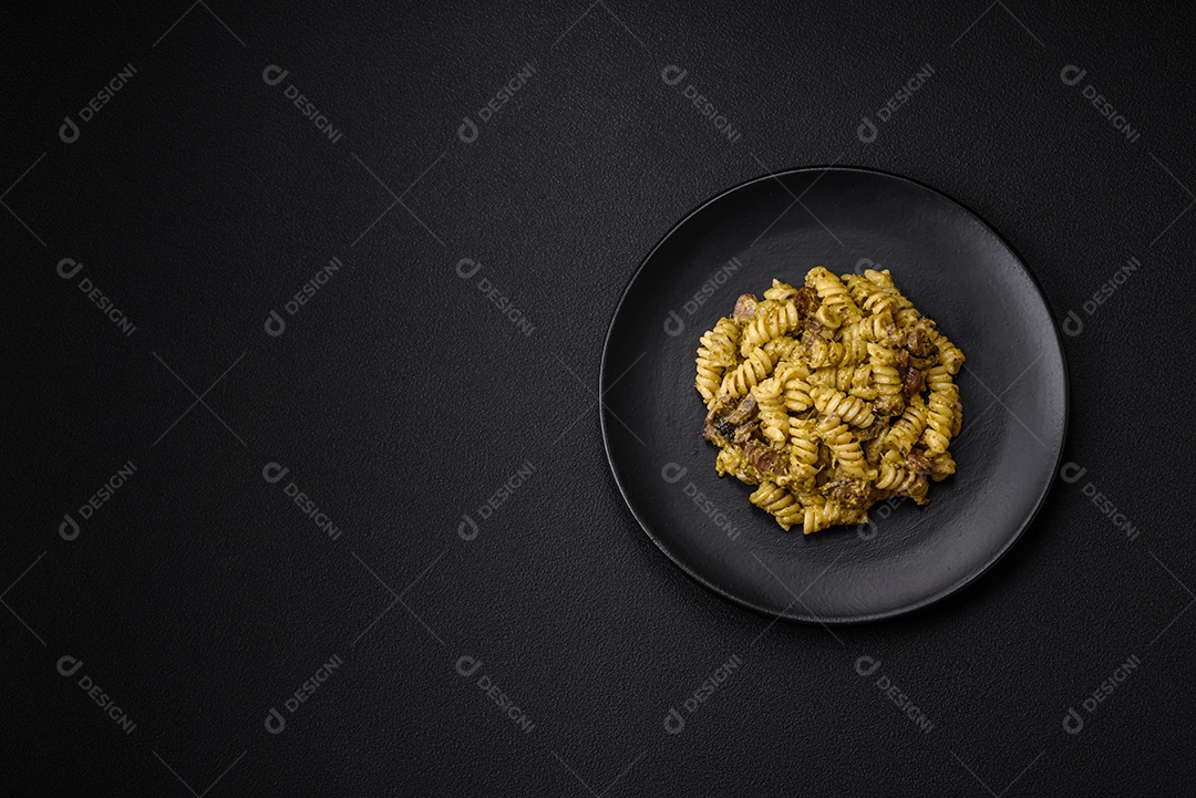 Deliciosa massa fusilli com molho pesto verde, com sal e especiarias num prato cerâmico sobre um fundo escuro de concreto