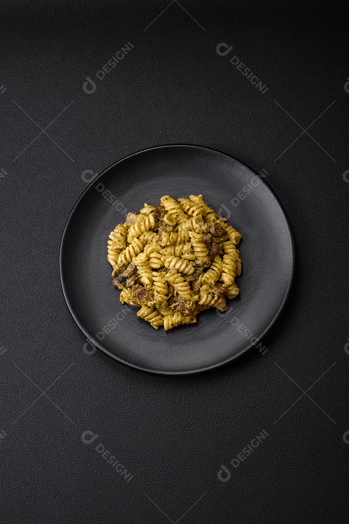 Deliciosa massa fusilli com molho pesto verde, com sal e especiarias num prato cerâmico sobre um fundo escuro de concreto