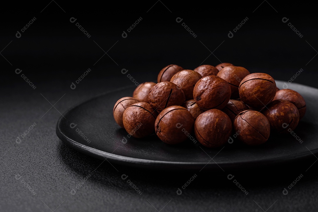 Deliciosas nozes de macadâmia torradas com casca sobre um fundo de concreto texturizado escuro. Comida vegetariana