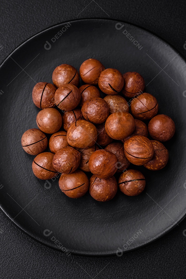 Deliciosas nozes de macadâmia torradas com casca sobre um fundo de concreto texturizado escuro. Comida vegetariana