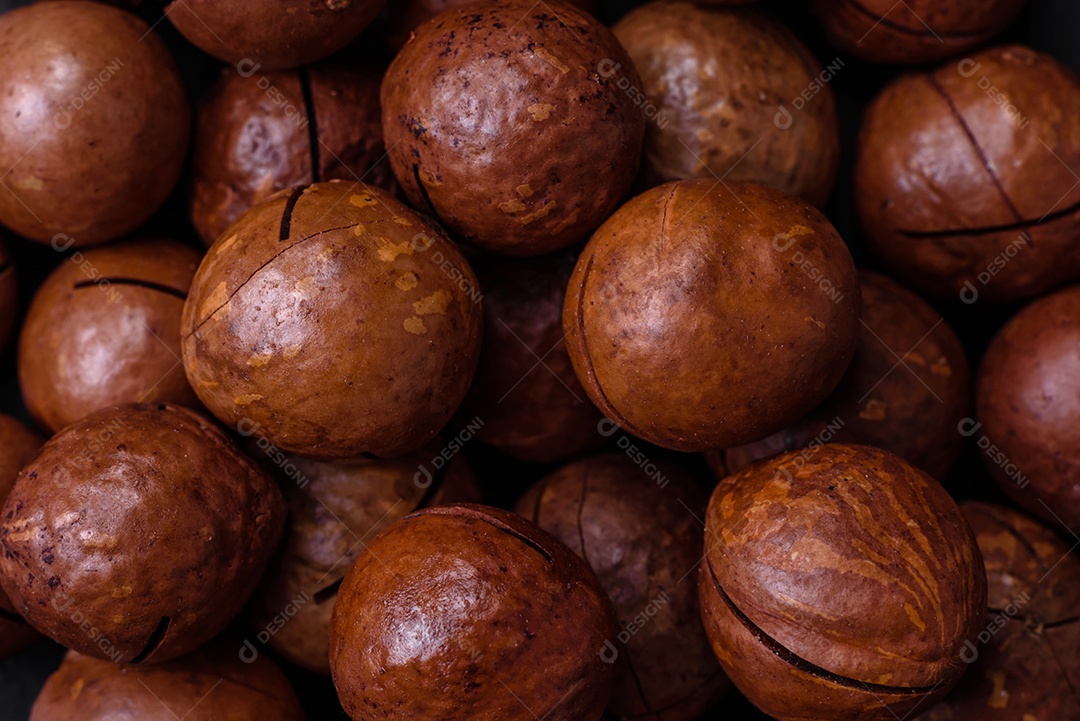 Deliciosas nozes de macadâmia torradas com casca sobre um fundo de concreto texturizado escuro. Comida vegetariana