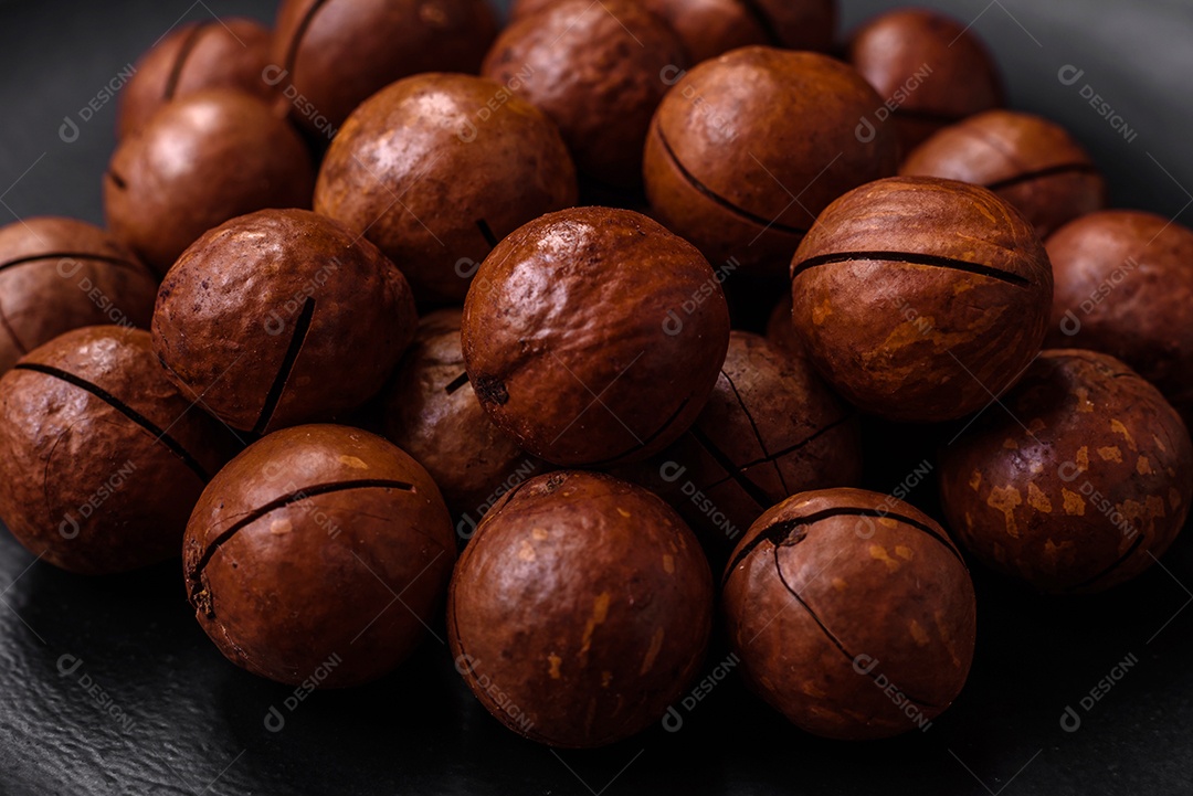 Deliciosas nozes de macadâmia torradas com casca sobre um fundo de concreto texturizado escuro. Comida vegetariana