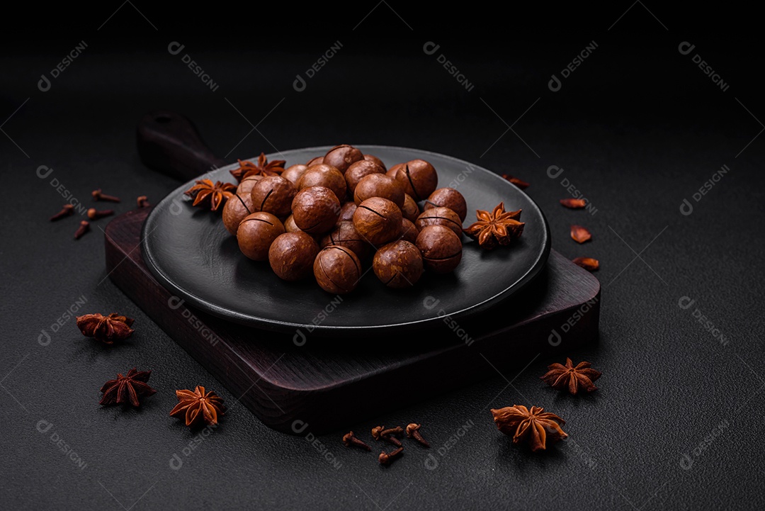 Deliciosas nozes de macadâmia torradas com casca sobre um fundo de concreto texturizado escuro. Comida vegetariana