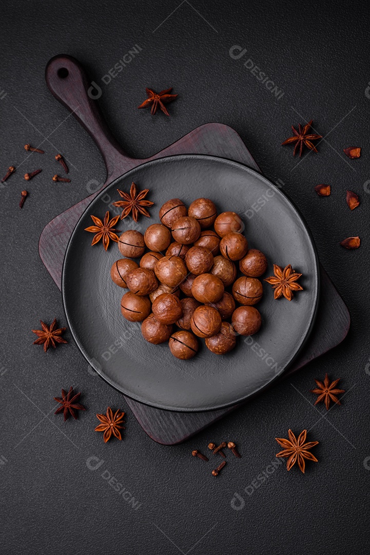 Deliciosas nozes de macadâmia torradas com casca sobre um fundo de concreto texturizado escuro. Comida vegetariana