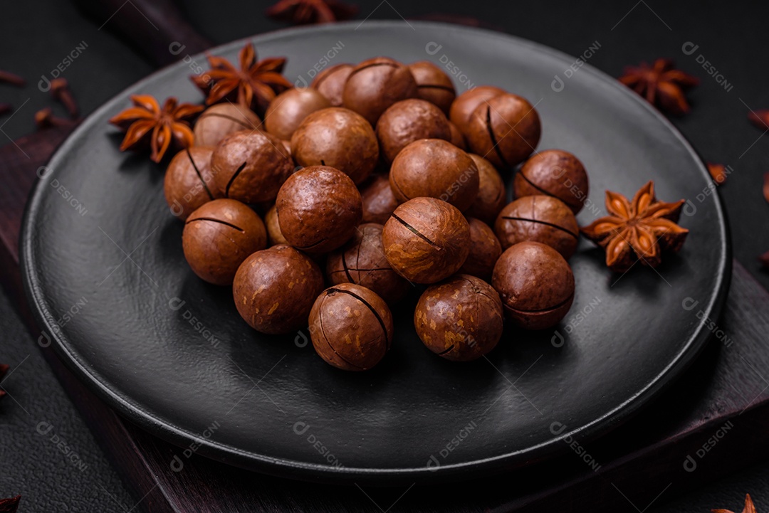 Deliciosas nozes de macadâmia torradas com casca sobre um fundo de concreto texturizado escuro. Comida vegetariana