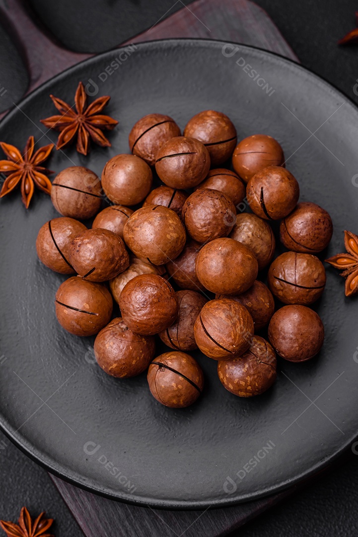 Deliciosas nozes de macadâmia torradas com casca sobre um fundo de concreto texturizado escuro. Comida vegetariana