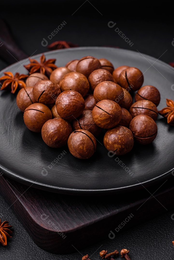 Deliciosas nozes de macadâmia torradas com casca sobre um fundo de concreto texturizado escuro. Comida vegetariana