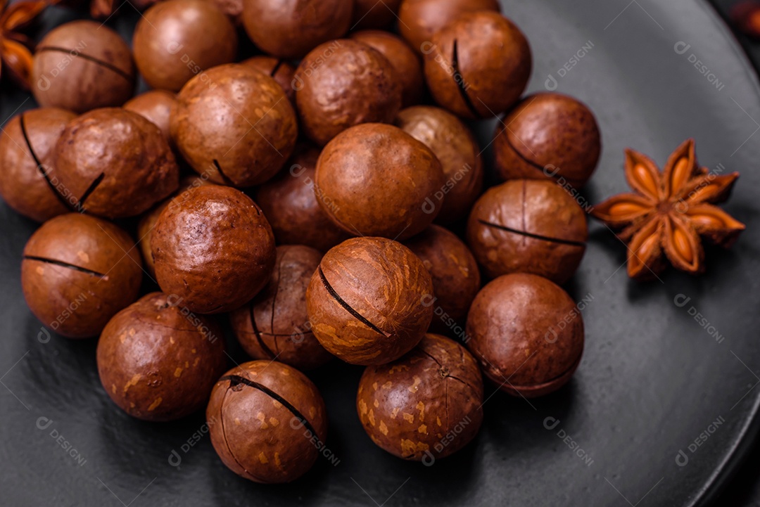 Deliciosas nozes de macadâmia torradas com casca sobre um fundo de concreto texturizado escuro. Comida vegetariana