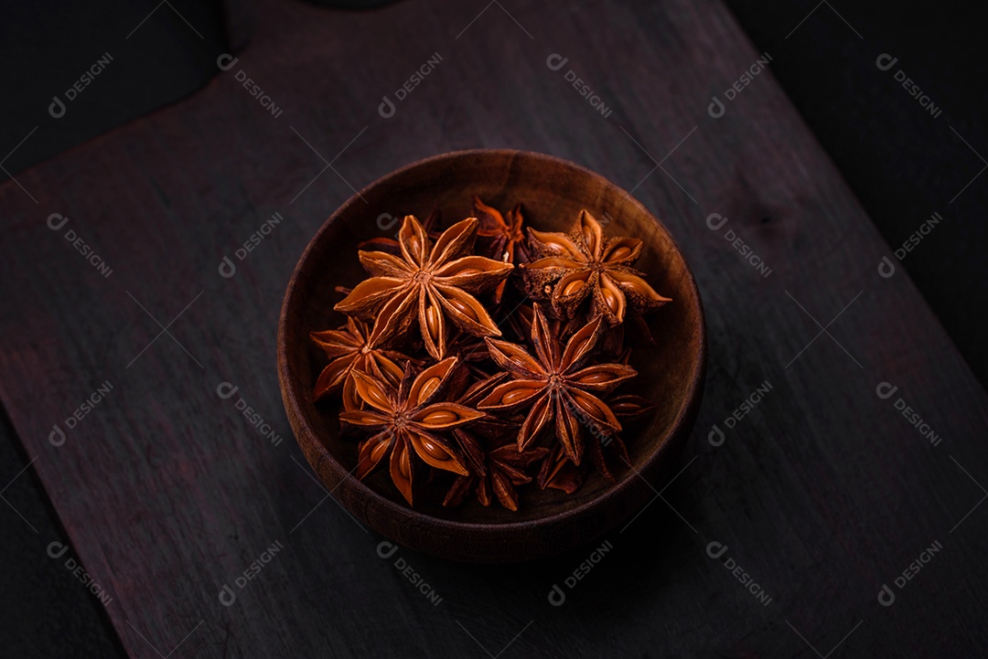 Anis estrelado em forma de estrela em uma tigela redonda de madeira sobre um fundo escuro de concreto