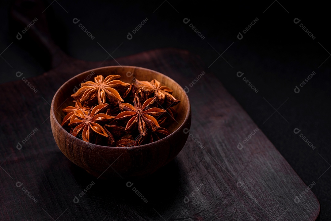 Anis estrelado em forma de estrela em uma tigela redonda de madeira sobre um fundo escuro de concreto