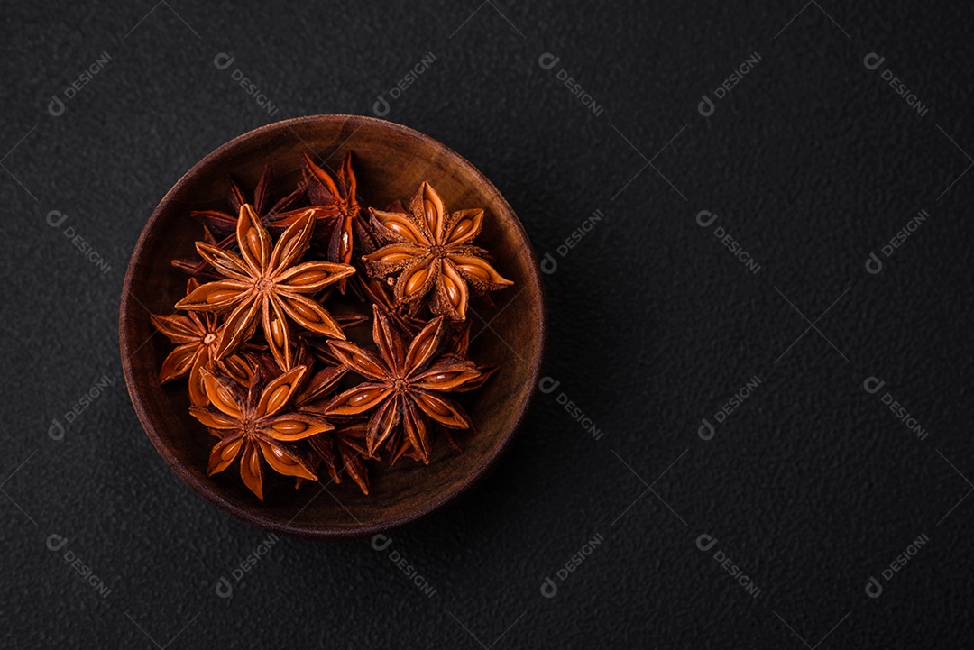 Anis estrelado em forma de estrela em uma tigela redonda de madeira sobre um fundo escuro de concreto