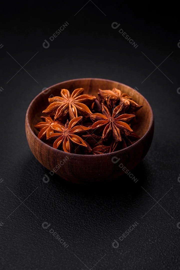 Anis estrelado em forma de estrela em uma tigela redonda de madeira sobre um fundo escuro de concreto